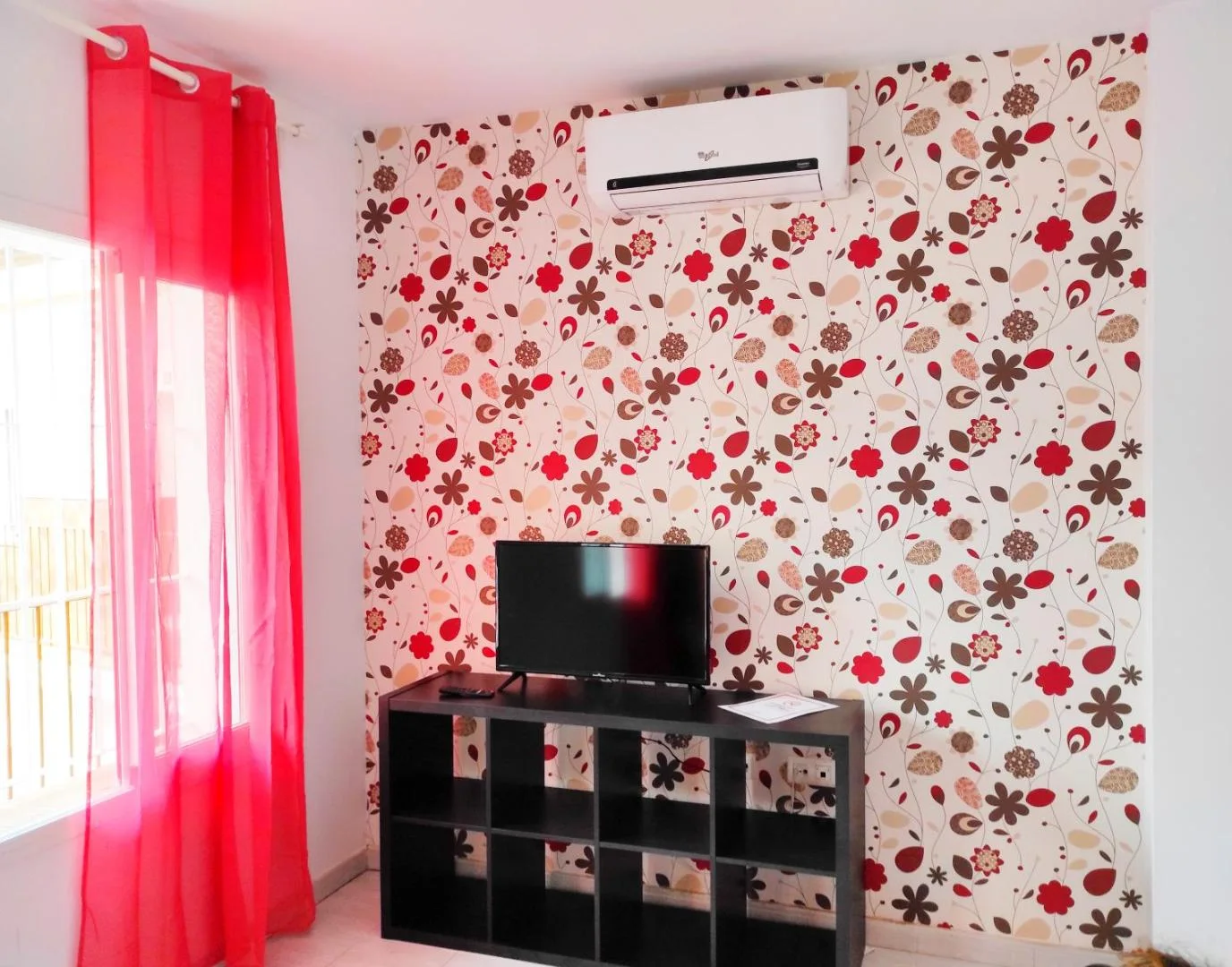 Zona de estar con televisión y papel pintado de flores